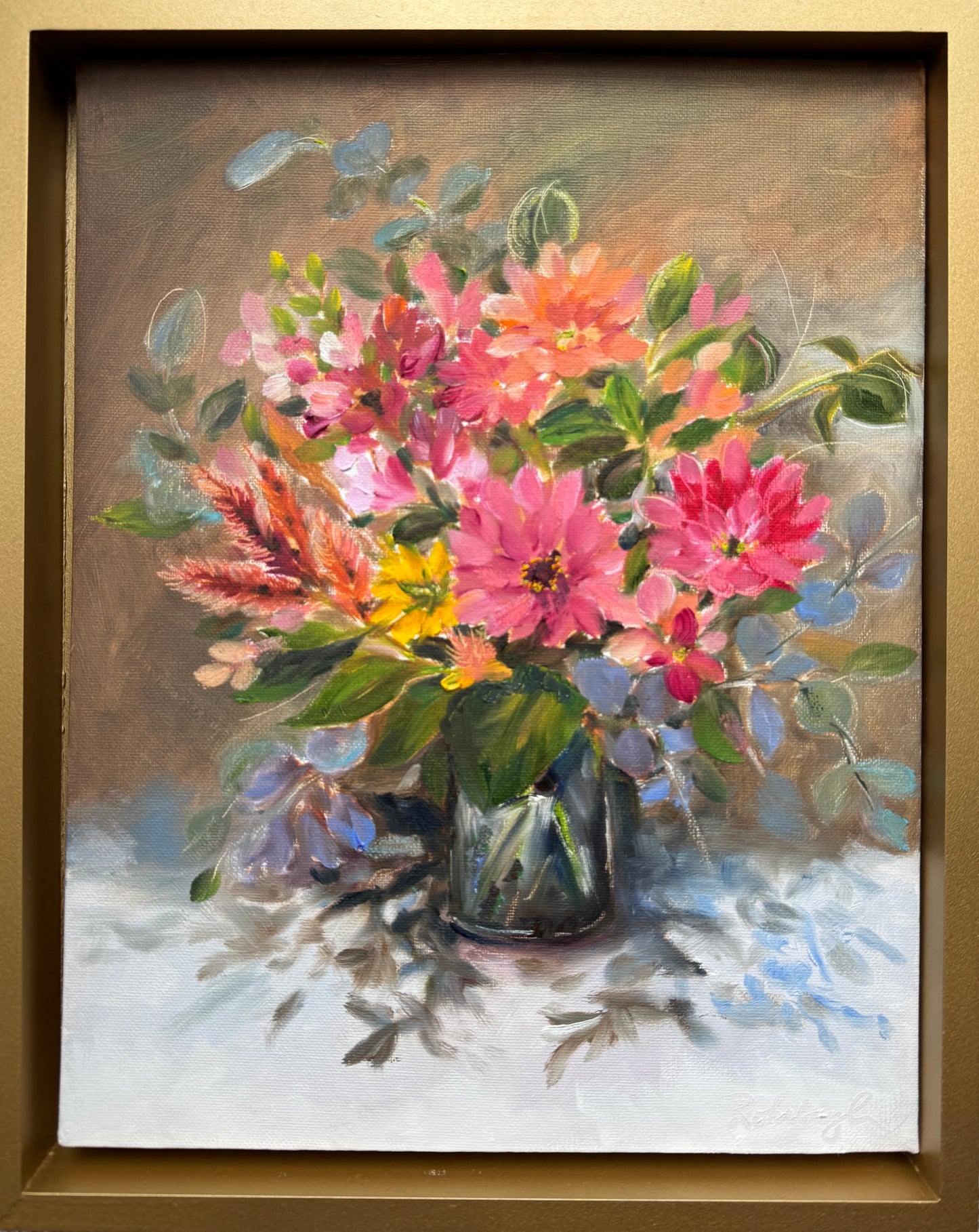 A colorful floral painting featuring a bouquet of flowers in warm corals and yellows, with green leaves, placed in a vase on a table. The artwork is framed in a gold floater frame.